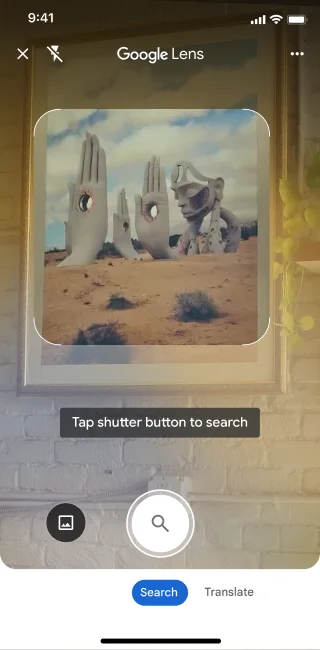 On a phone, the Google Lens app is open. A notification indicates that the user can tap the shutter button to search an image of large stone hand sculptures in a desert.